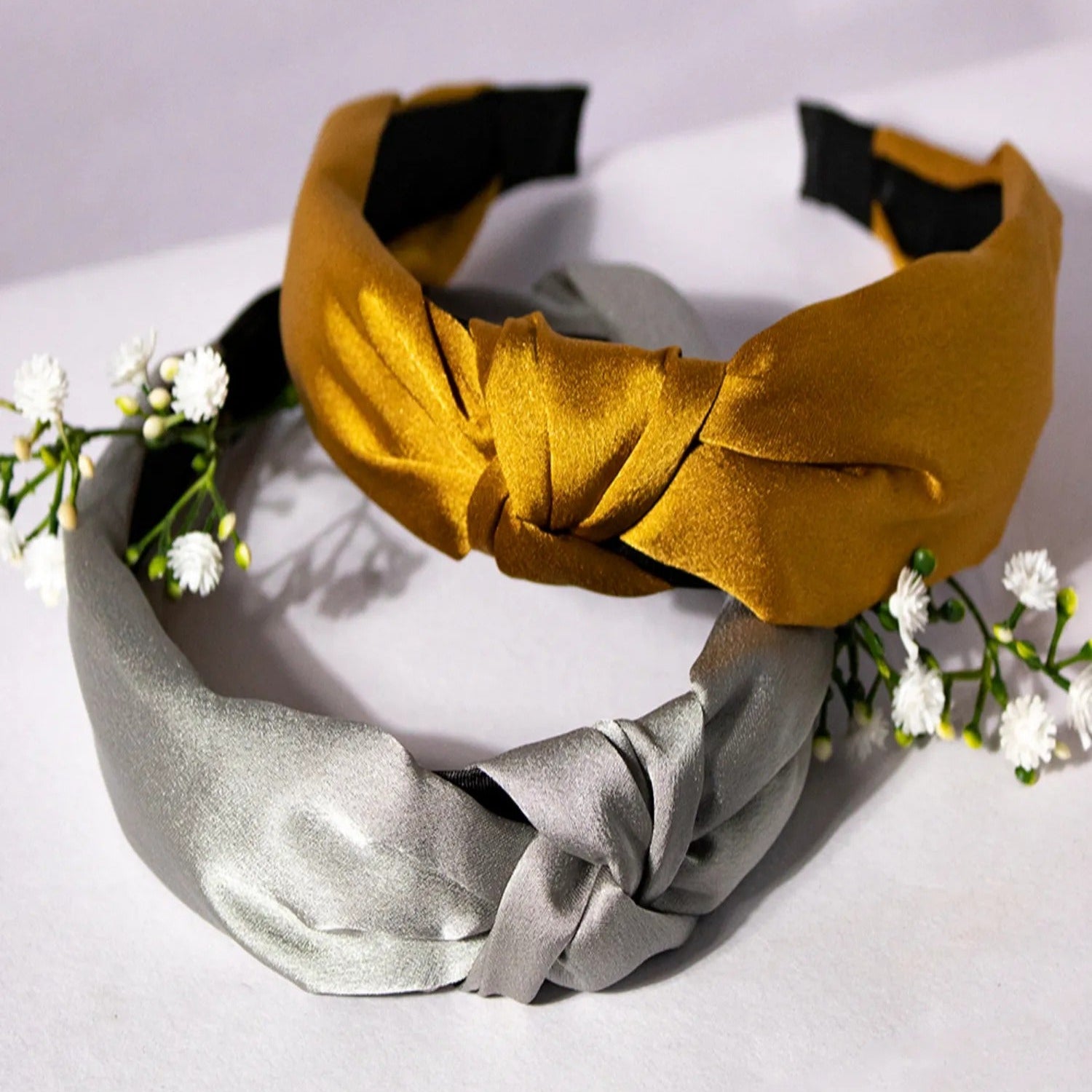 Mustard and silver headbands on a white surface with small white flowers.