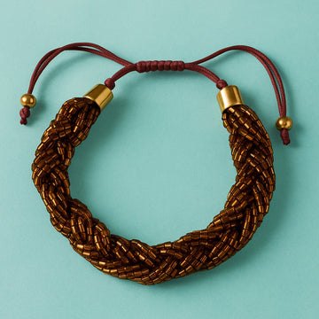 Brown braided bracelet with gold accents on a light blue background
