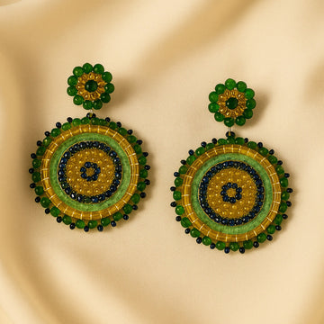 Pair of round beaded earrings with green, gold, and black on a beige fabric background