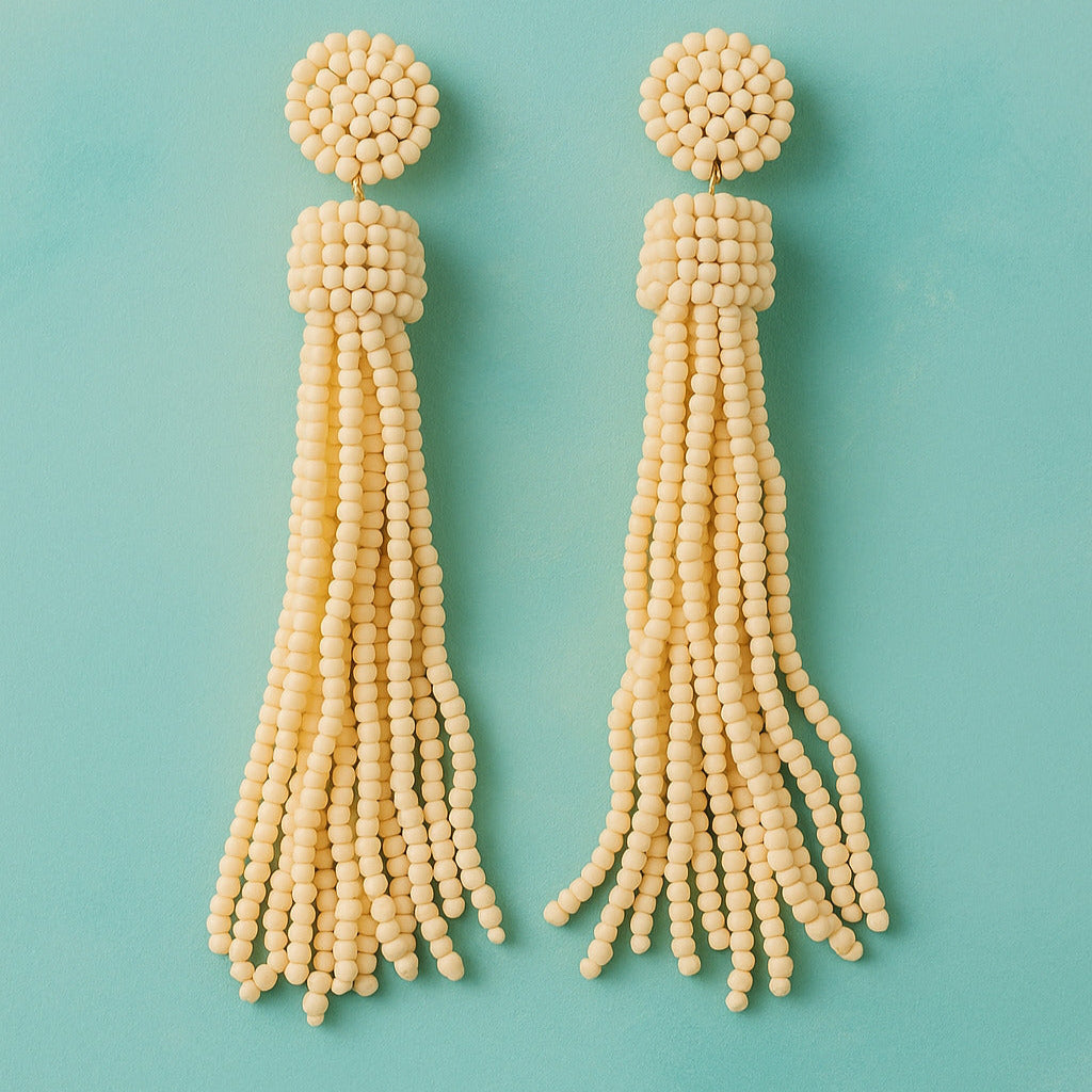 Pair of beige beaded tassel earrings on a teal background