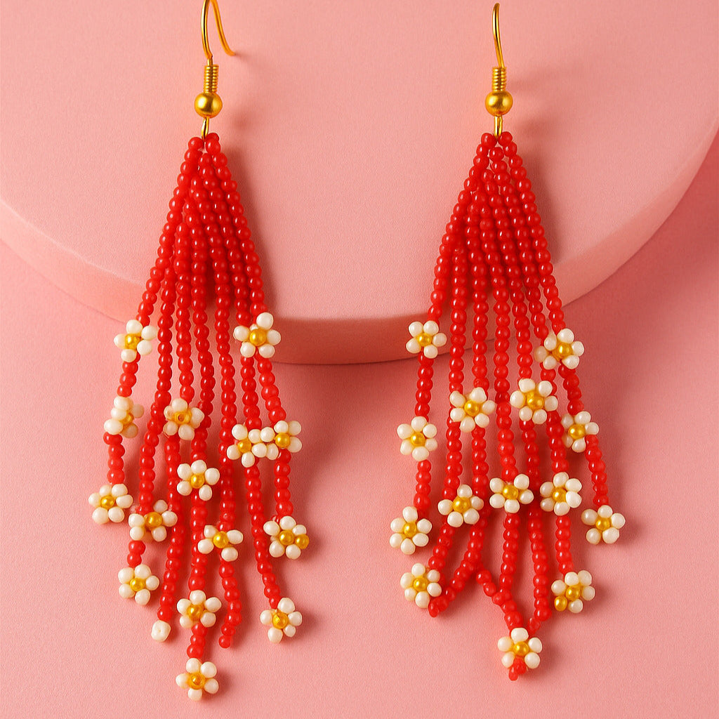 Red beaded earrings with white and gold accents on a pink background