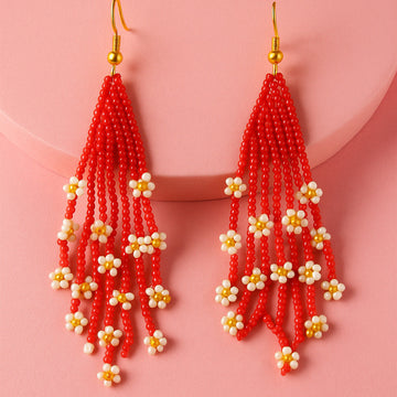 Red beaded earrings with white and gold accents on a pink background
