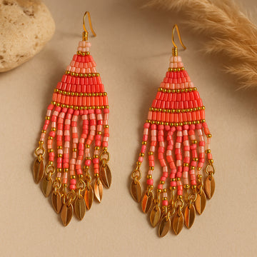 Pair of pink beaded earrings with gold accents on a beige background