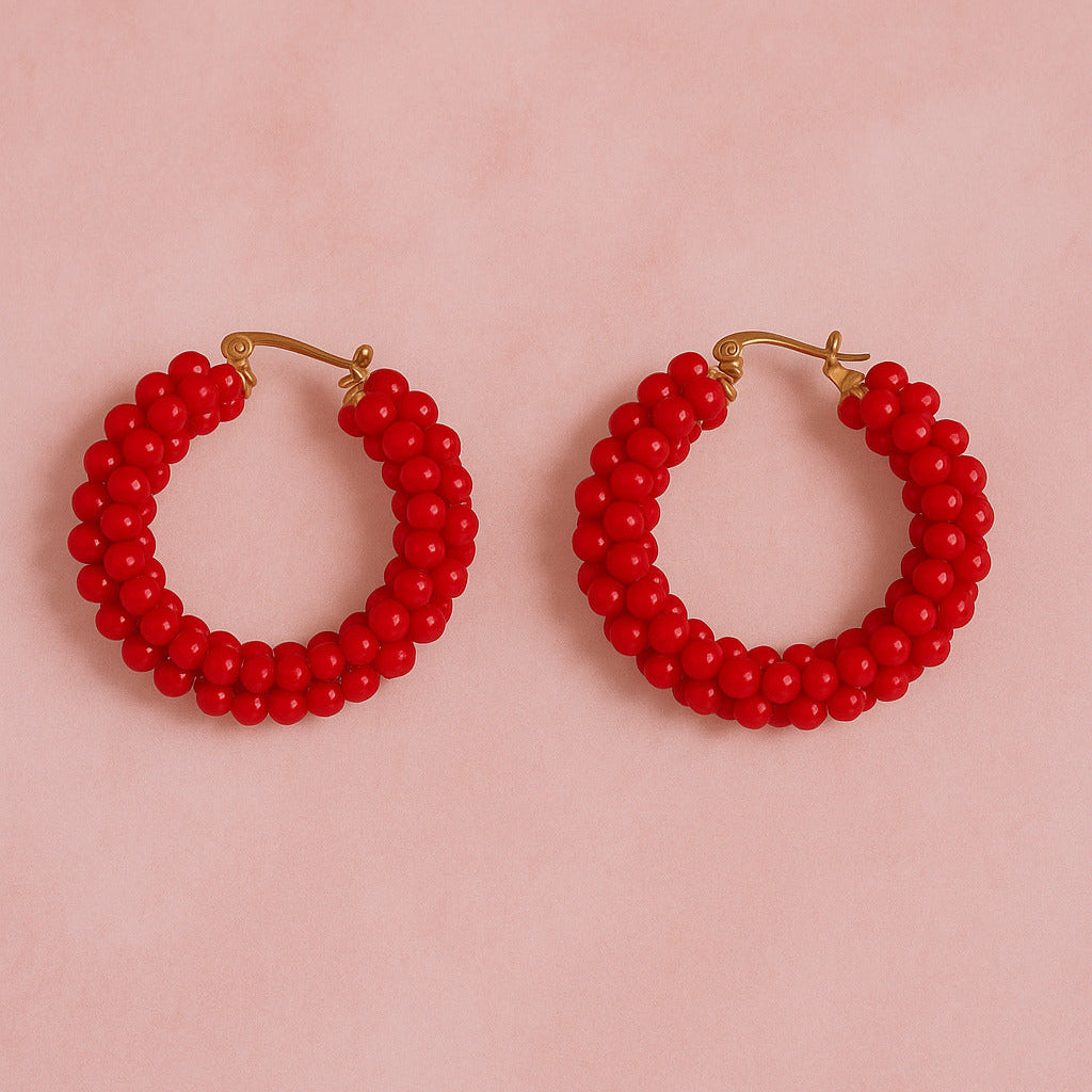 Red beaded hoop earrings on a pink background