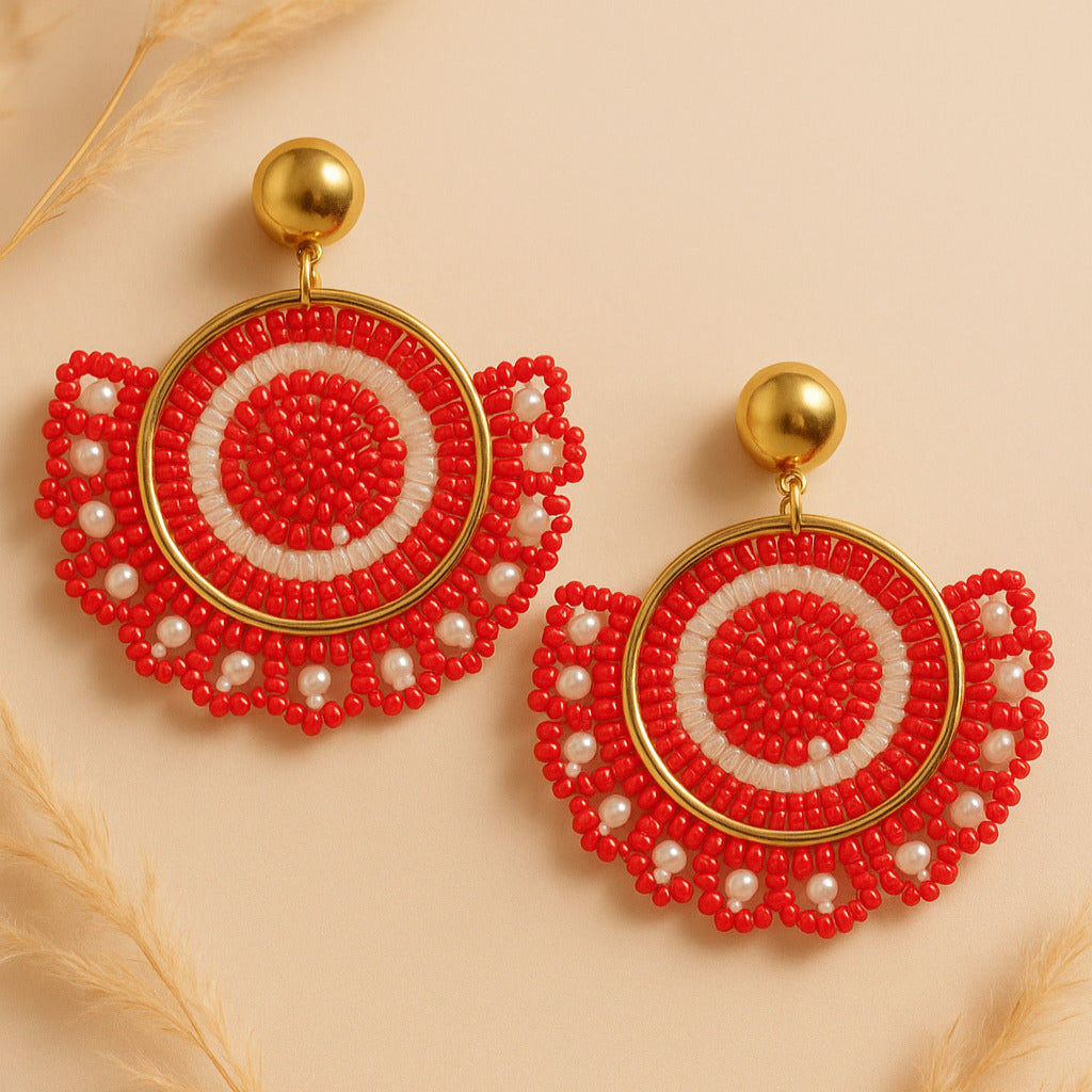 Pair of red beaded earrings with gold accents on a beige background