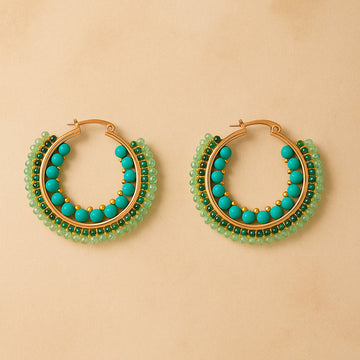 Gold hoop earrings with turquoise and green beads on a beige background