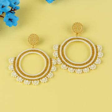 Pair of gold and white beaded earrings on a yellow background with blue flowers.