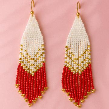 Beaded earrings with white, gold, and red design on a pink background