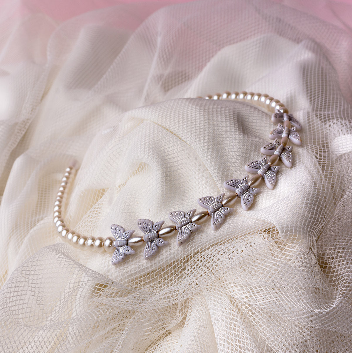A white hairband with butterfly-shaped embellishments and imitation pearl beads, displayed on a textured fabric.