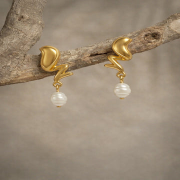 Gold earrings with pearl drops on a branch against a neutral background