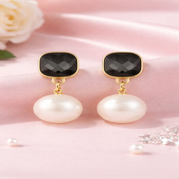 Pair of earrings with black stones and pearls on a pink background
