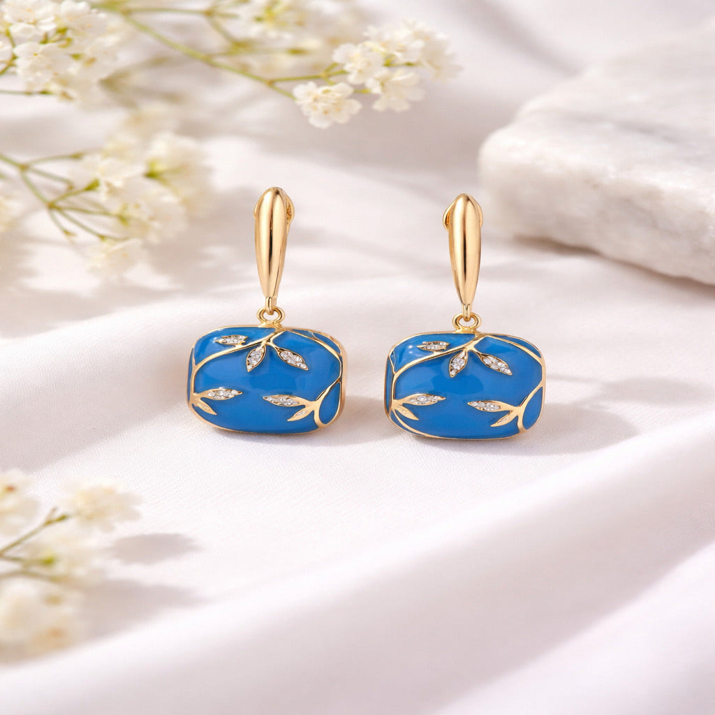 Blue earrings with gold accents on a white fabric background with flowers.