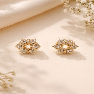 Gold earrings with clear stones on a beige surface with floral elements