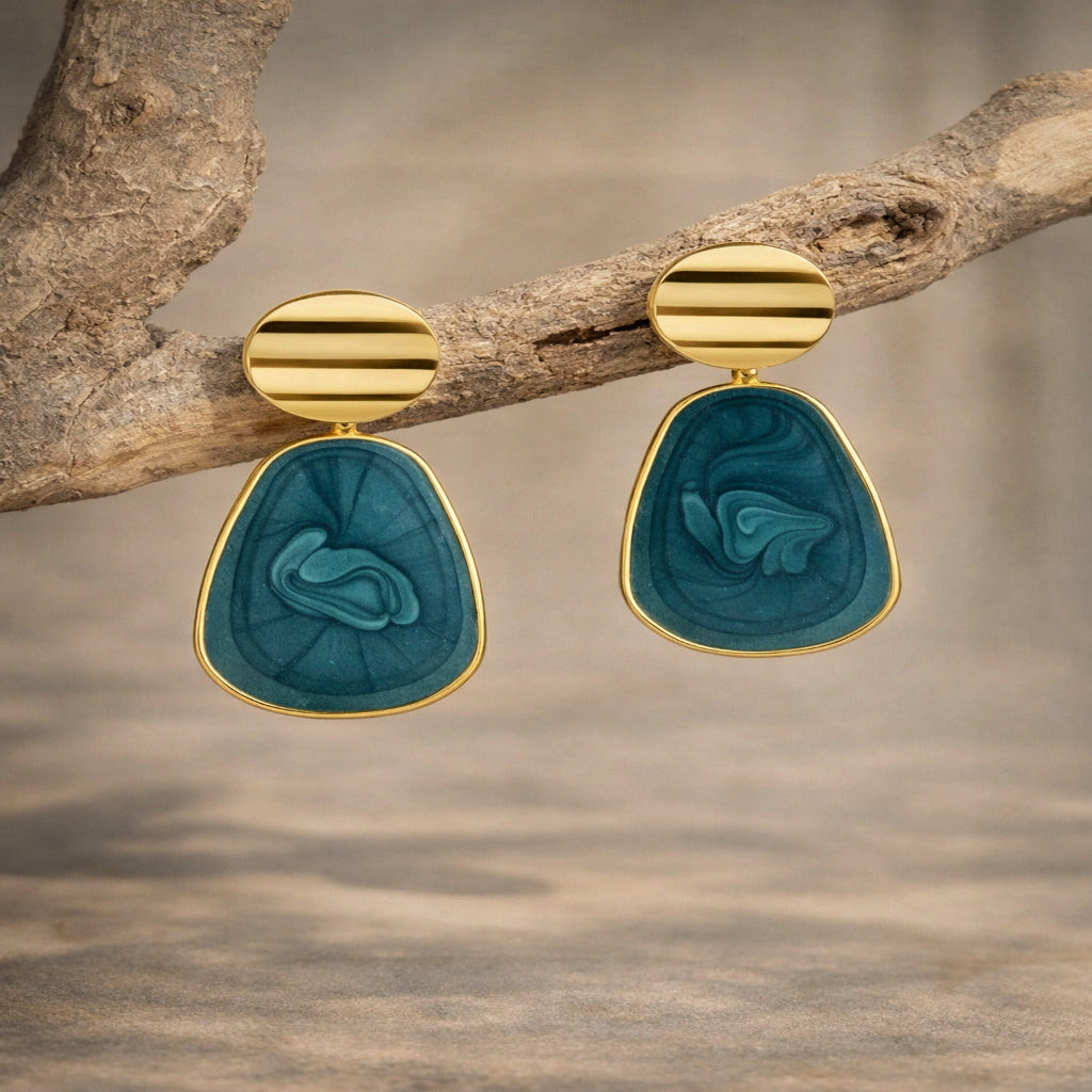 Gold and teal earrings hanging on a branch with a natural background