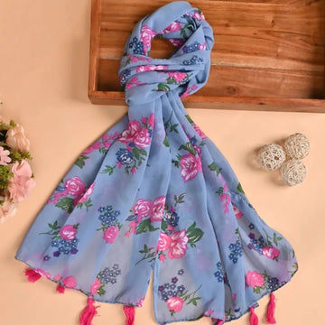 A blue silk stole with a printed floral design and pink tassels, displayed on a wooden surface with flowers around it.