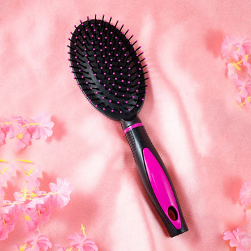 A plastic hair comb with black bristles and a pink handle, presented on a pink background with floral designs.