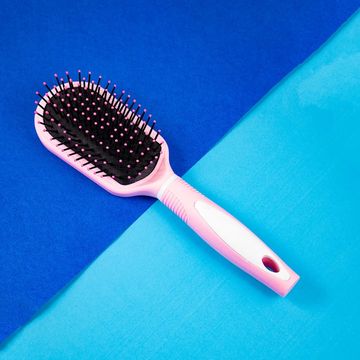 A pink plastic hair brush with black bristles, placed on a blue background.