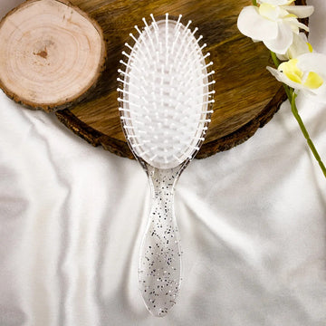 A white plastic hair comb with a scalp-friendly design, featuring rounded tips to prevent scalp irritation, placed on a wooden surface with a flower beside it.