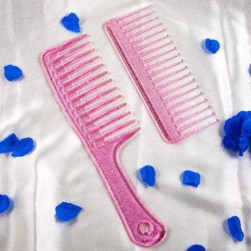 Two pink plastic hair combs with a glittery finish, one with teeth in a vertical orientation and the other in a horizontal orientation, displayed on a white background with blue decorative hearts around them.