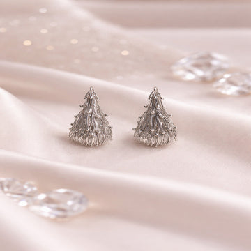 Silver tree-shaped earrings on a soft pink fabric background