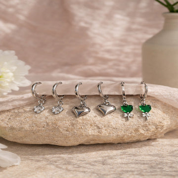Set of silver and green earrings on a stone surface with a soft background