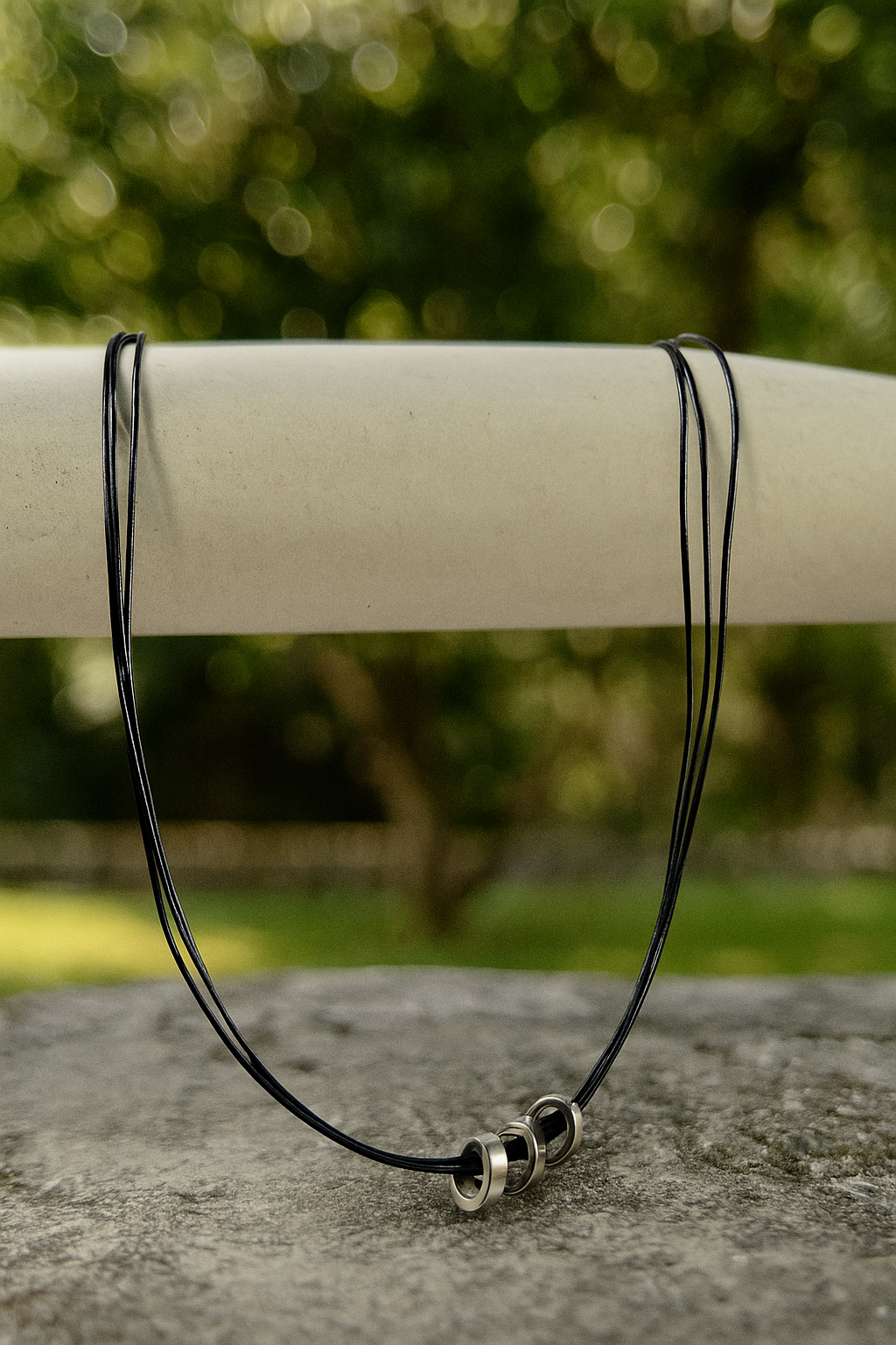 Black cord necklace with metal clasps on a stone surface with a blurred green background