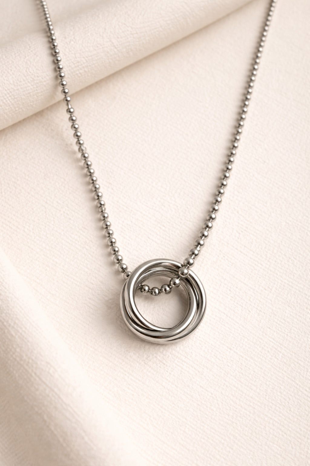 Silver necklace with a circular pendant on a light beige fabric background