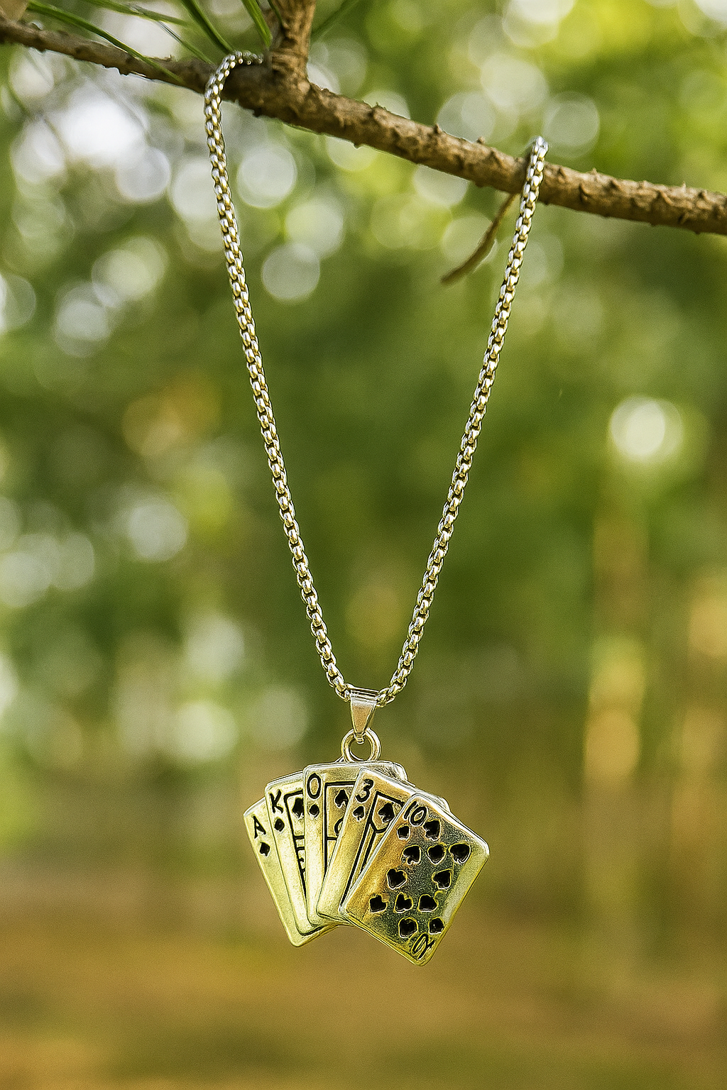 Necklace with a pendant shaped like playing cards hanging from a branch with a blurred green background