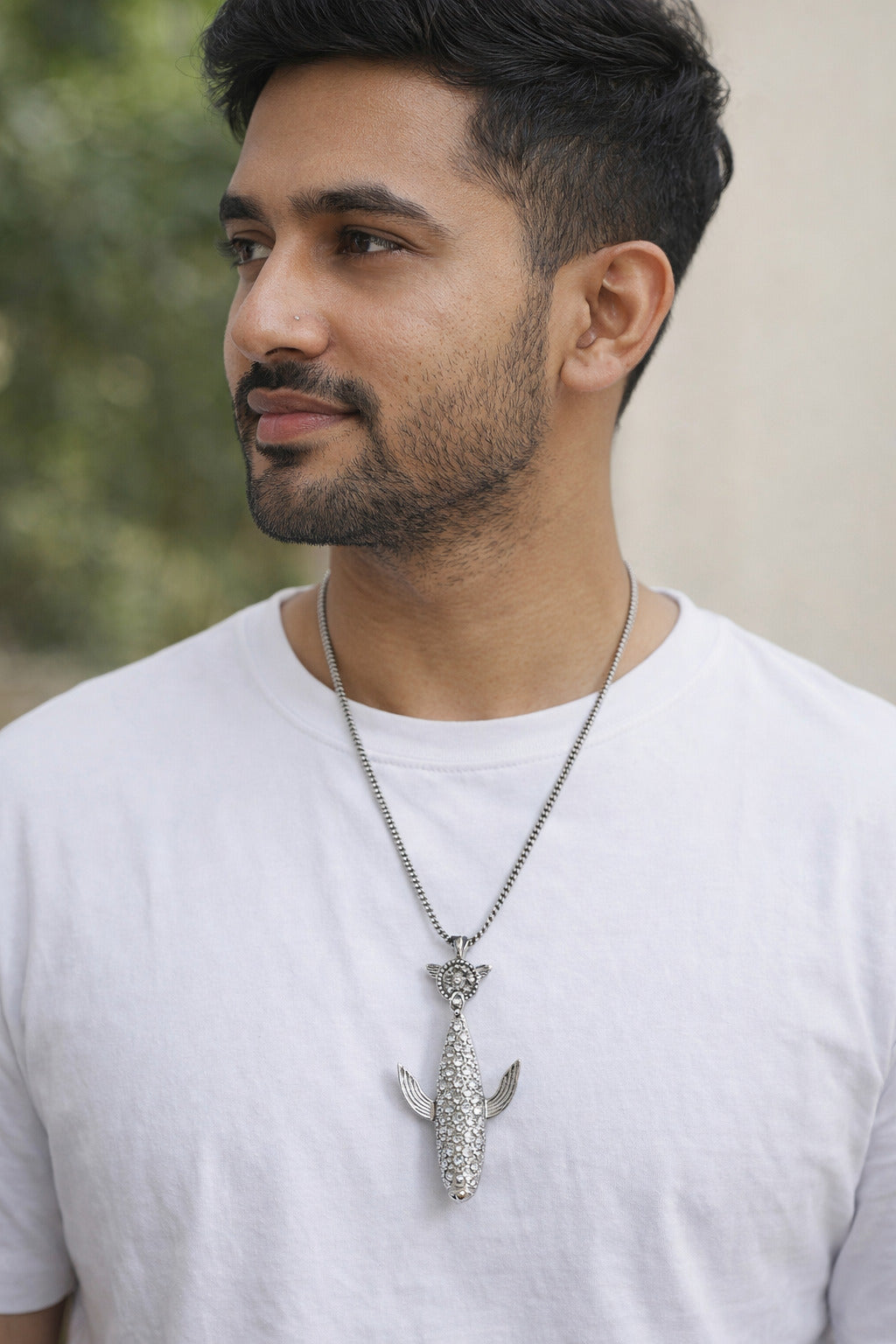 Man wearing a white t-shirt with a decorative necklace featuring a fish pendant.