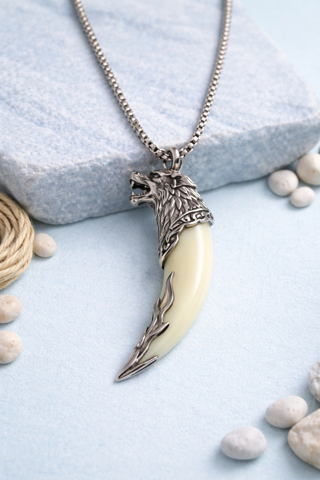Necklace with a wolf head pendant and tusk on a light blue surface with pebbles.