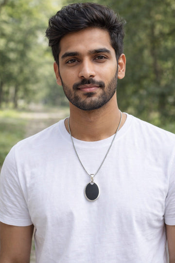 Man wearing a white t-shirt and necklace with a blurred green background