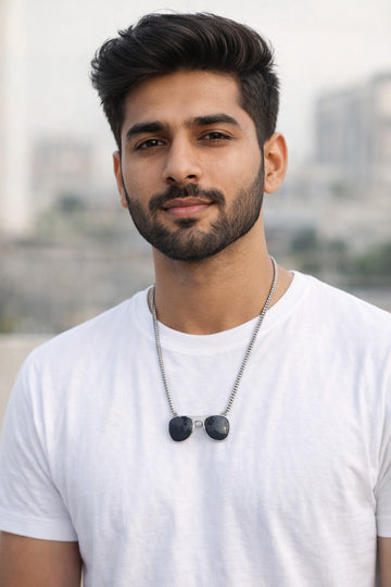 Man wearing a white t-shirt and necklace with a blurred cityscape background