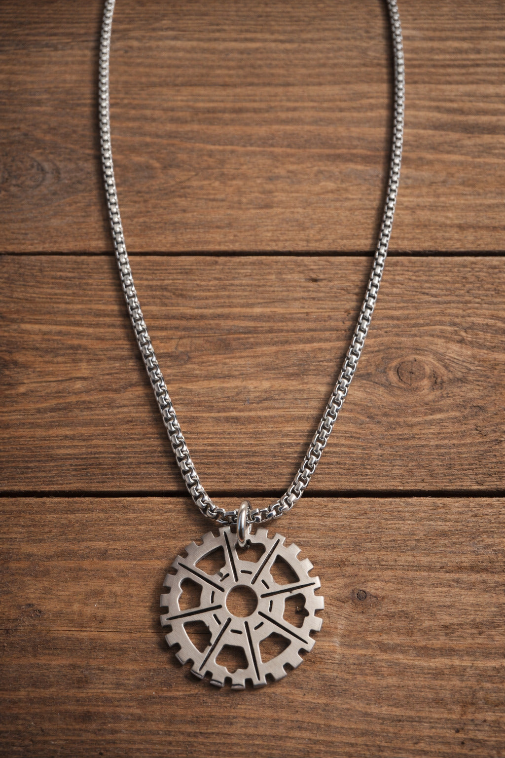 Silver necklace with a gear-shaped pendant on a wooden surface