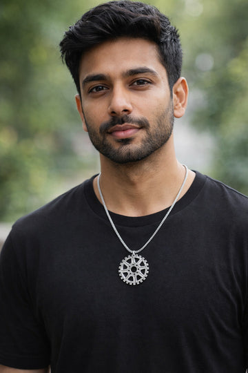 Man wearing a black t-shirt and silver necklace with a gear design, standing outdoors.