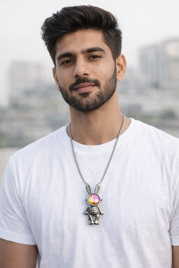 Man wearing a white t-shirt with a colorful pendant necklace against a blurred outdoor background
