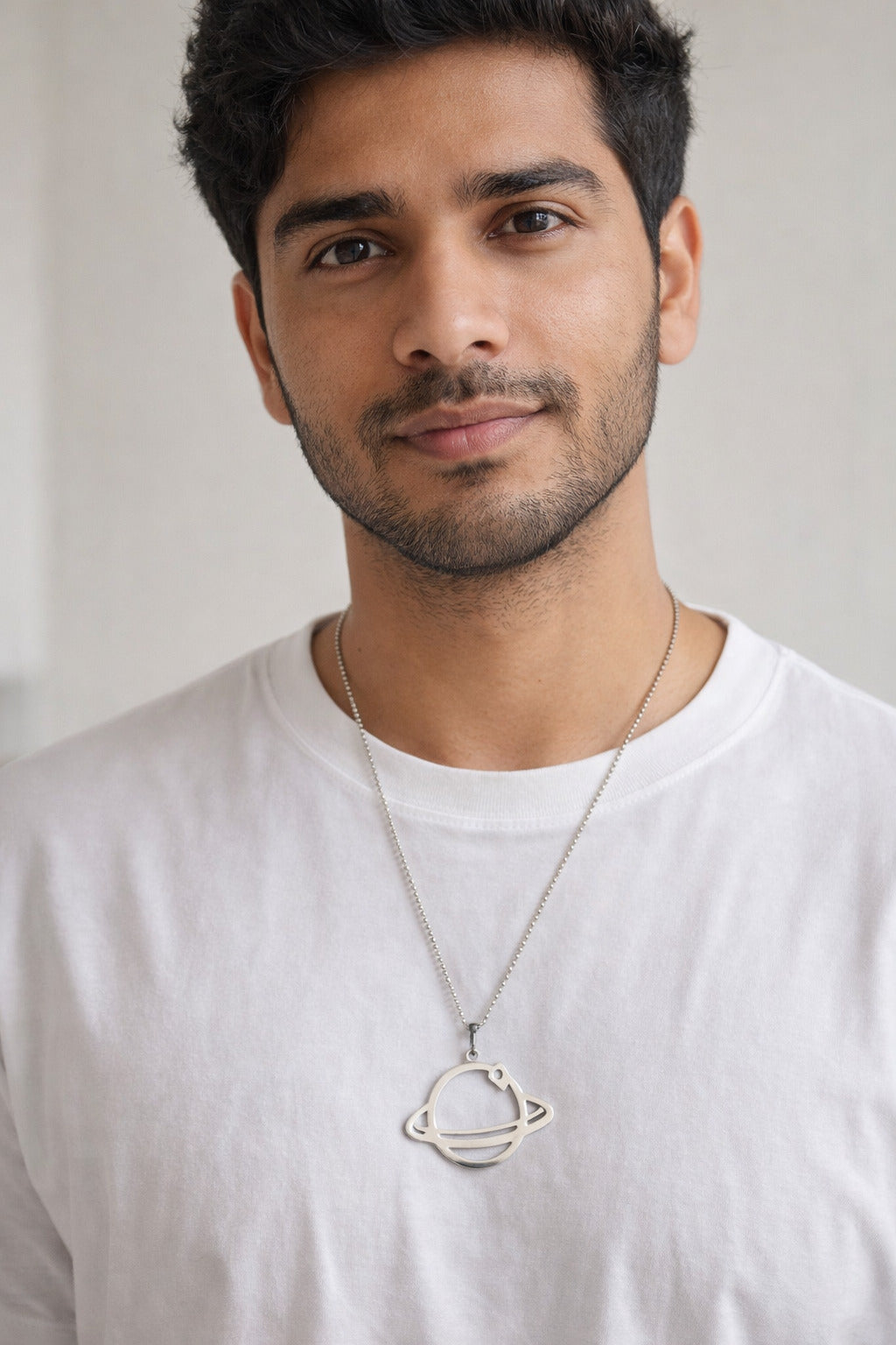 Man wearing a white t-shirt and a necklace with a planet pendant against a plain background