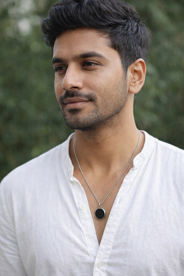 Man wearing a white shirt and necklace with a blurred green background