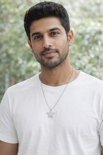 Man wearing a white t-shirt and star-shaped necklace with a blurred green background