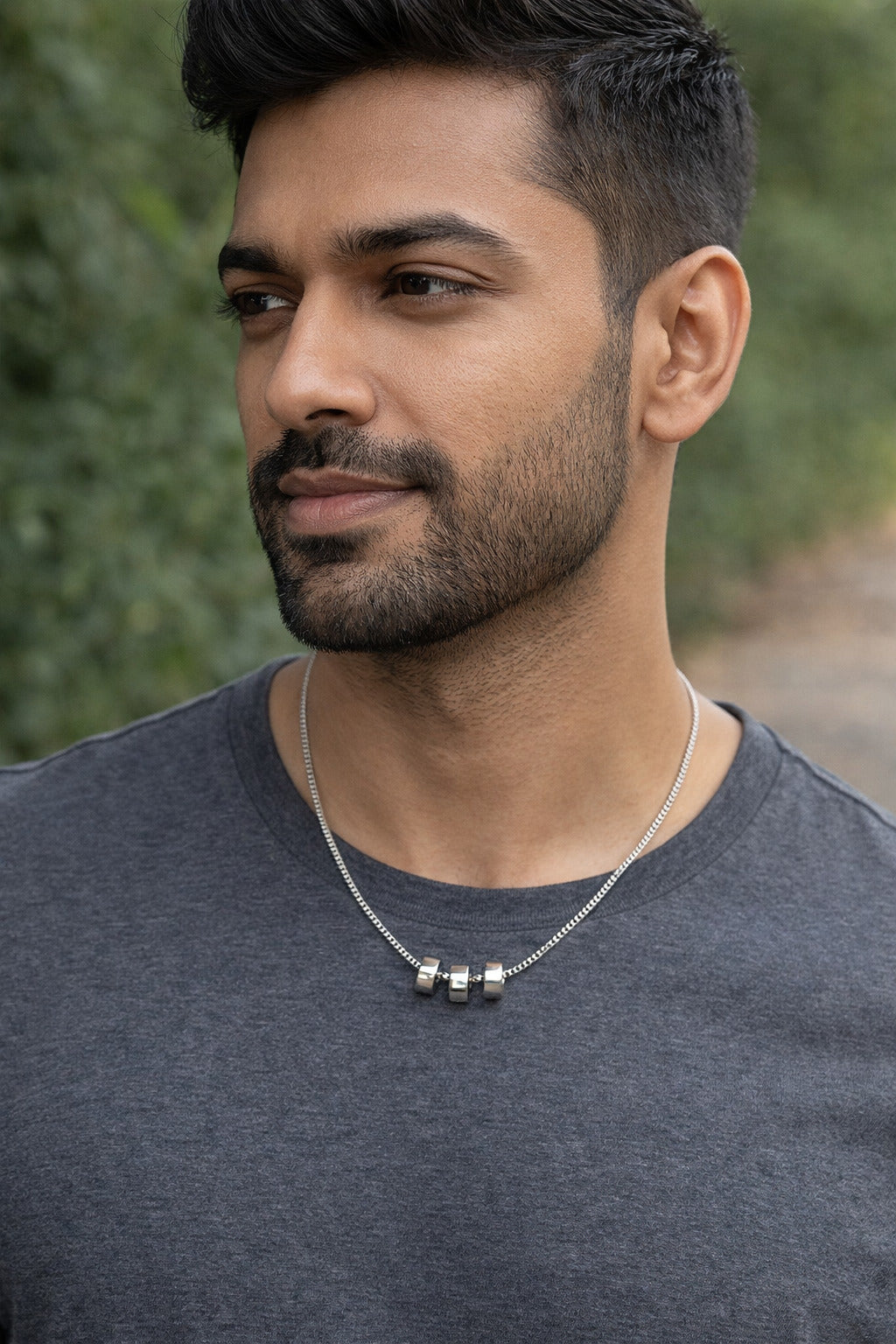 Man wearing a gray shirt and necklace with a blurred green background
