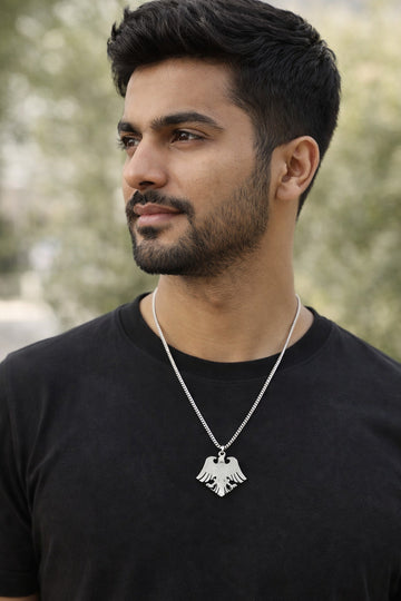 Man wearing a black shirt and silver necklace with an eagle pendant outdoors