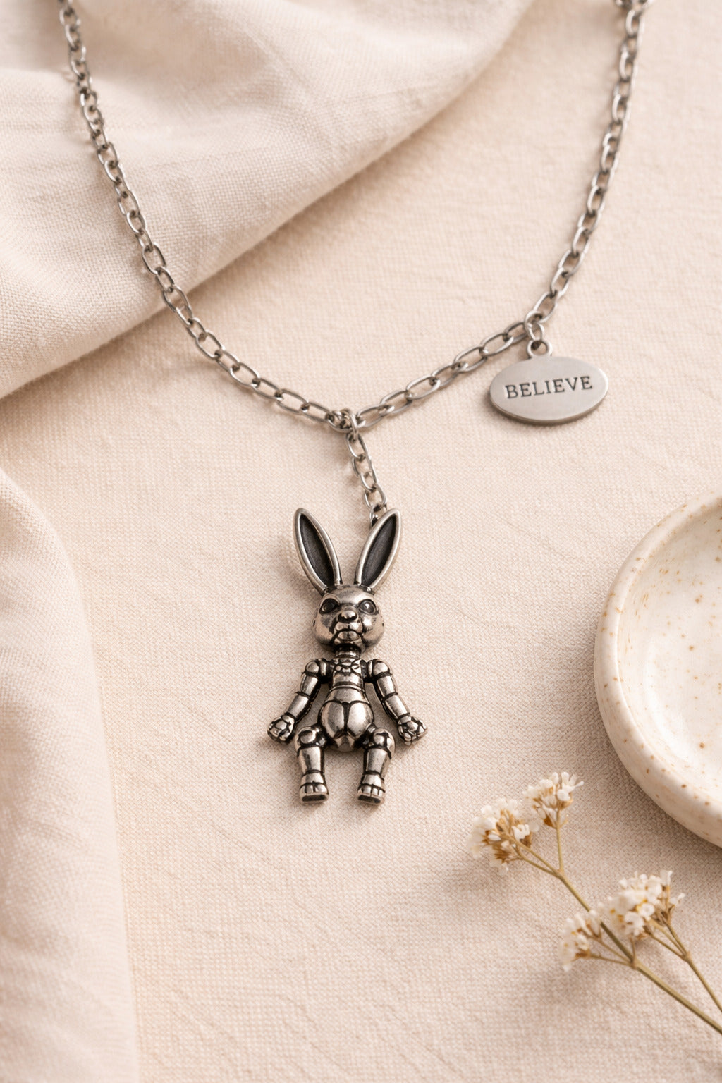 Necklace with a rabbit pendant and 'BELIEVE' tag on a beige fabric background