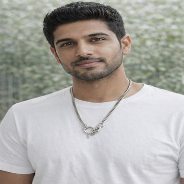 Man wearing a white t-shirt and necklace with a blurred natural background