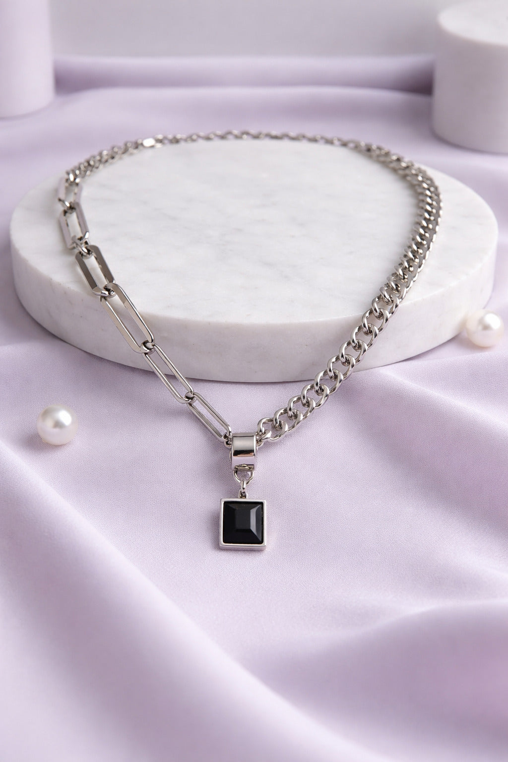 Silver chain necklace with a black pendant on a light purple fabric background