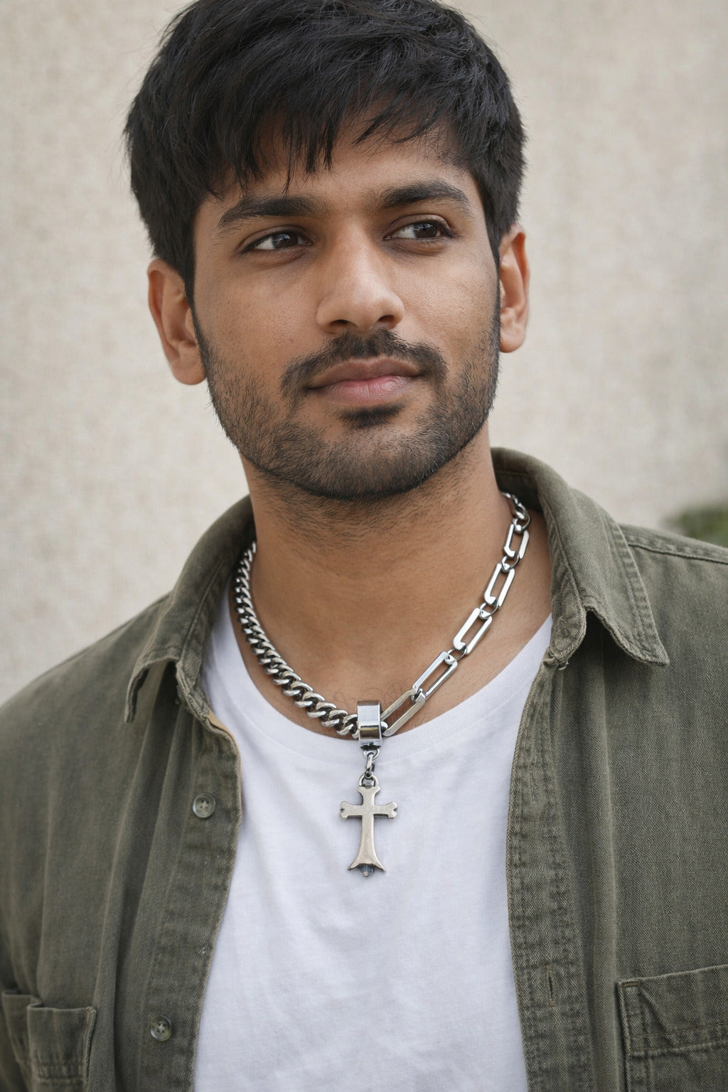 Man wearing a green jacket and white shirt with a necklace featuring a cross pendant.