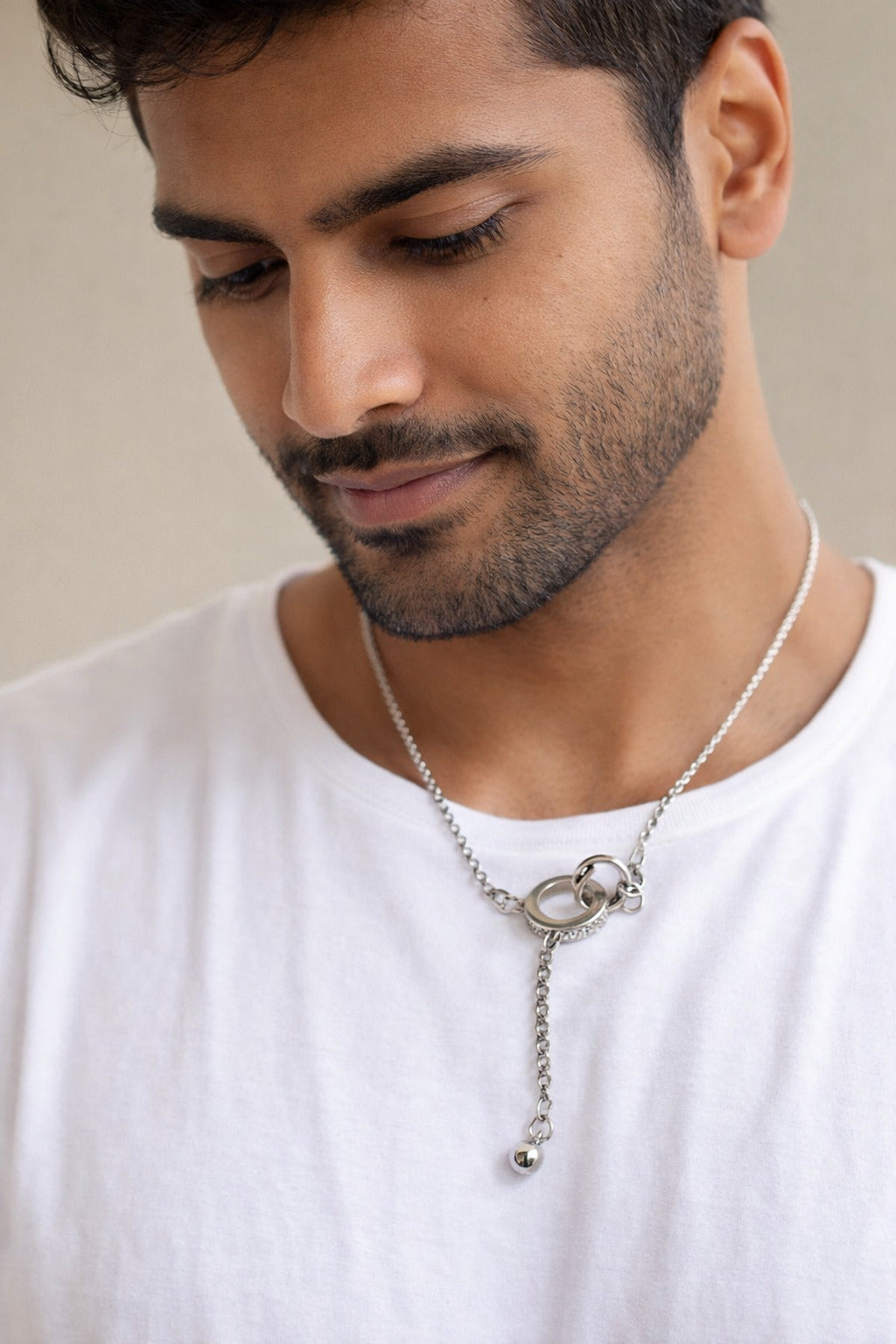 Man wearing a silver necklace with a neutral background