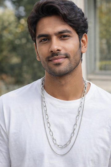 Man wearing a white shirt and silver chain necklace with a blurred outdoor background
