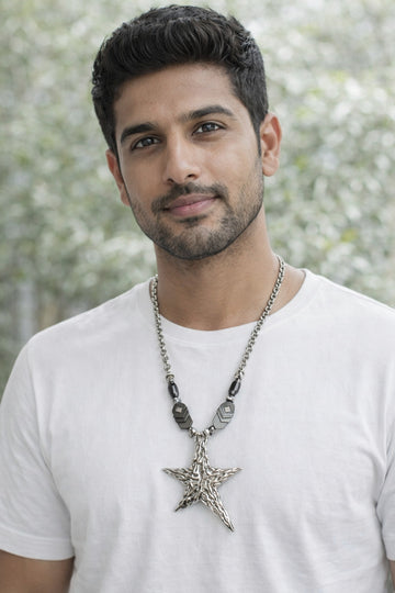 Man wearing a white t-shirt and a necklace with a star pendant against a blurred natural background