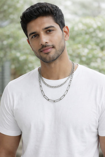 Man wearing a white t-shirt and multiple chain necklaces with a blurred natural background