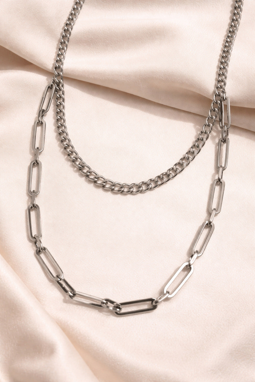Two silver chain necklaces on a beige fabric background
