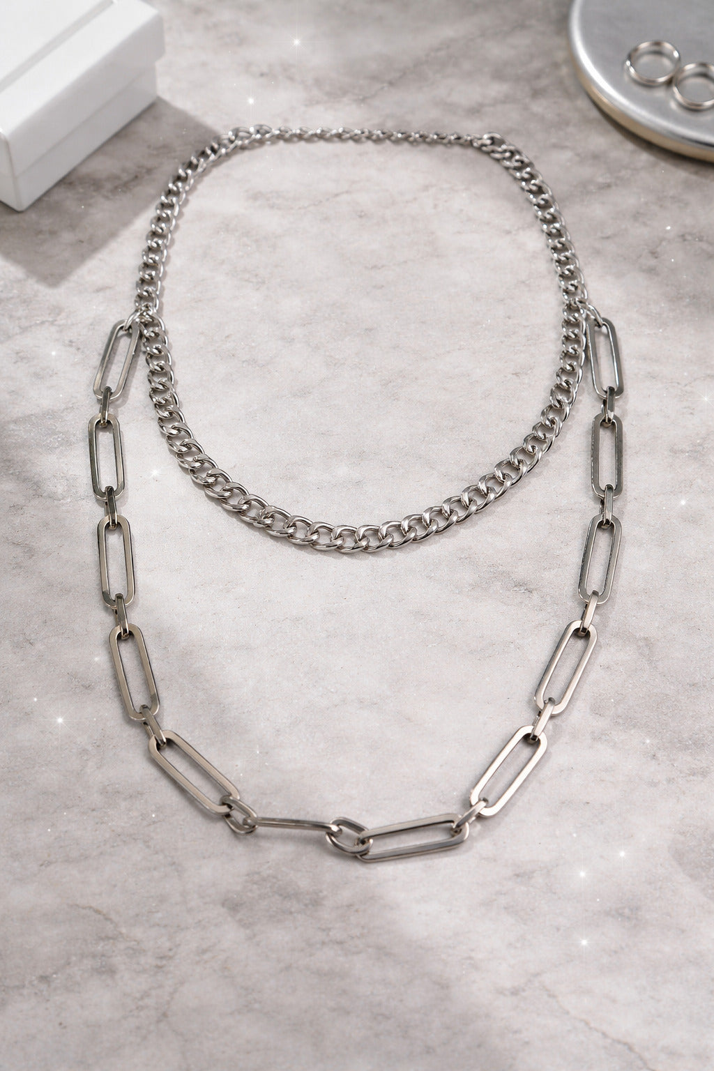 Two silver chain necklaces on a gray marble surface